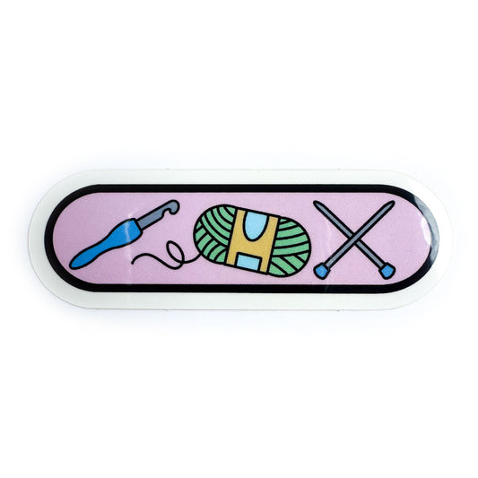 A bandaid shaped sticker with illustrations of a crochet hook, knitting needles, and a yarn ball on a pastel pink background.