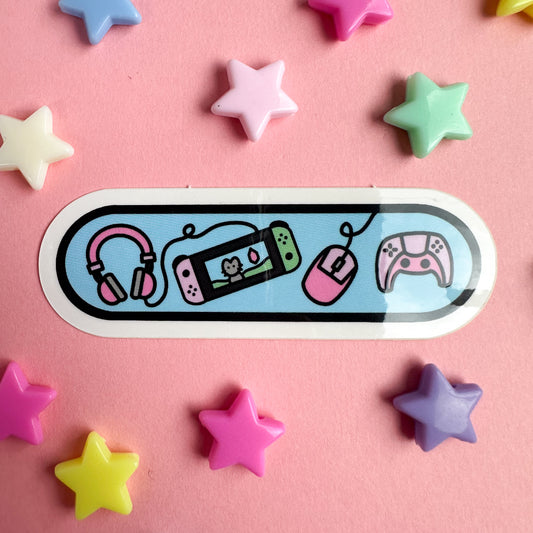 A blue capsule shaped sticker with cartoony illustrations of video game equipment on it. The sticker is on a pastel pink background with star beads around it.