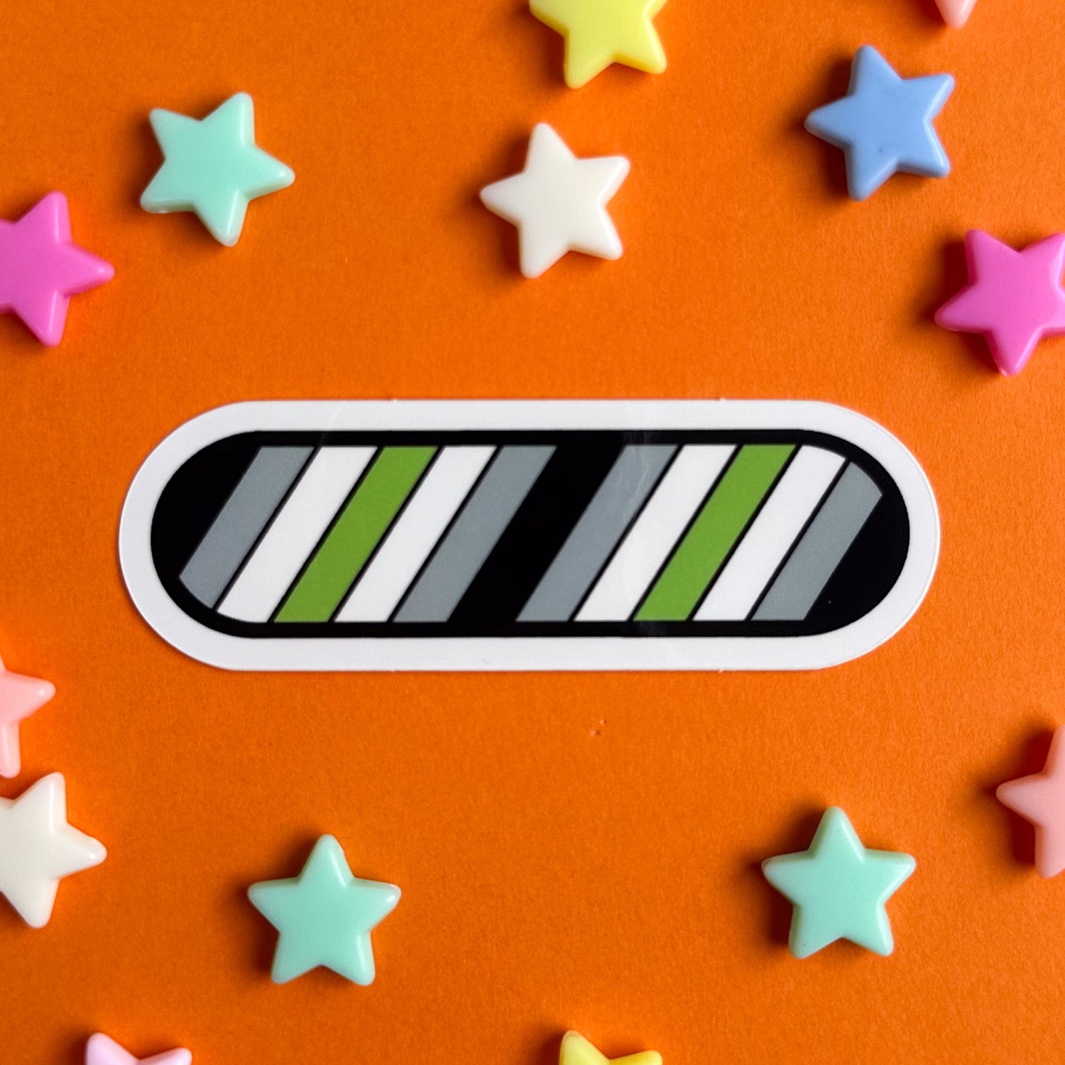 A vinyl sticker in the colors of the Agender flag. The sticker is on an orange background with star beads around it. 