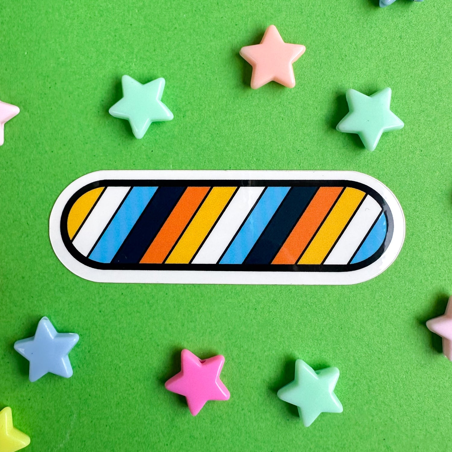 A capsule shaped sticker with the colors of the Aroace pride flag in diagonal stripes across it.