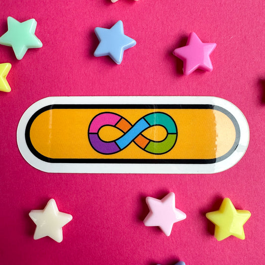 A capsule shaped sticker with the image of the Autistic Pride Flag on it, a rainbow infinity symbol with a gold background. The sticker is on a hot pink paper background with star beads strewn around it.
