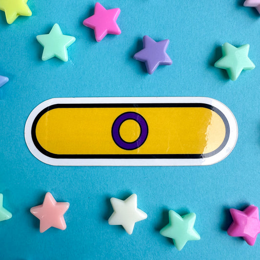 A vinyl sticker with a yellow background and purple circle in it to represent the Intersex Pride Flag. The sticker is on a blue background with pastel star beads around it.