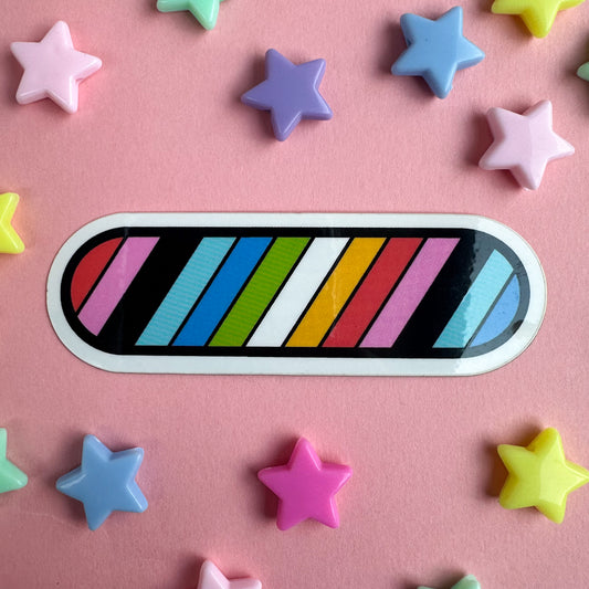 A capsule shaped sticker with diagonal stripes in the colors of the Queer Pride Flag. The sticker is on a pastel pink background with plastic star beads around it. 