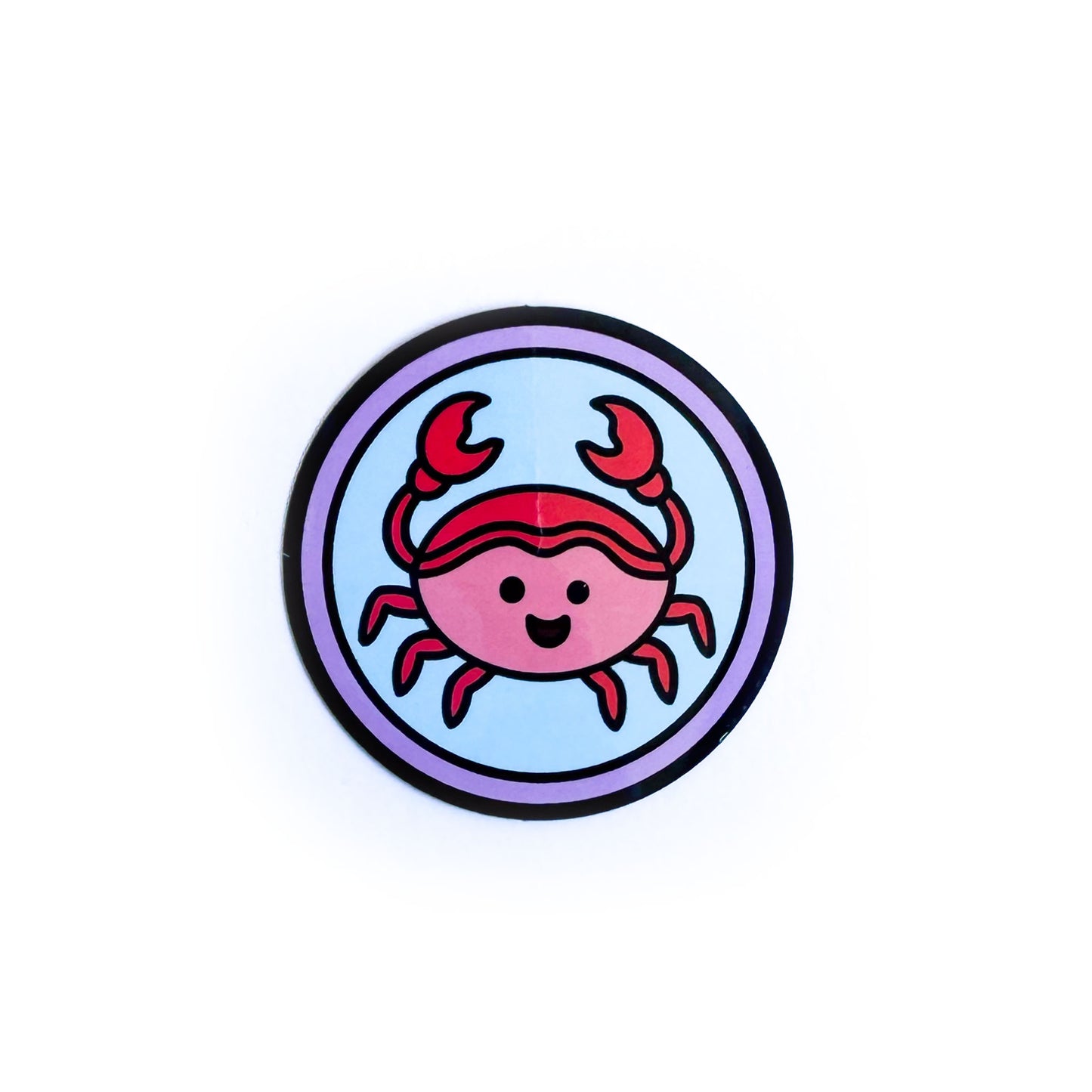 A circular sticker with a cute crab illustration to represent the Cancer zodiac sign in it with a blue background and purple border circle. 