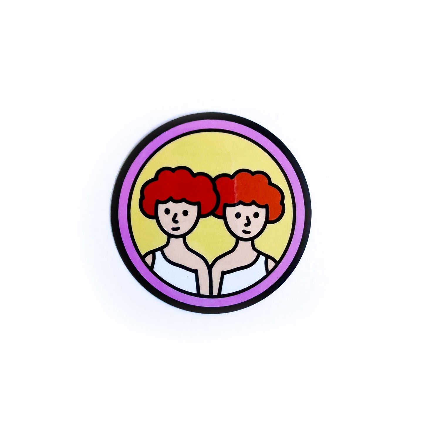 A circular sticker with twins with red hair on it to represent the Gemini Zodiac sign. 