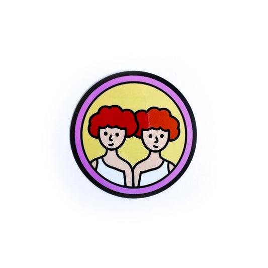 A circular sticker with twins with red hair on it to represent the Gemini Zodiac sign.