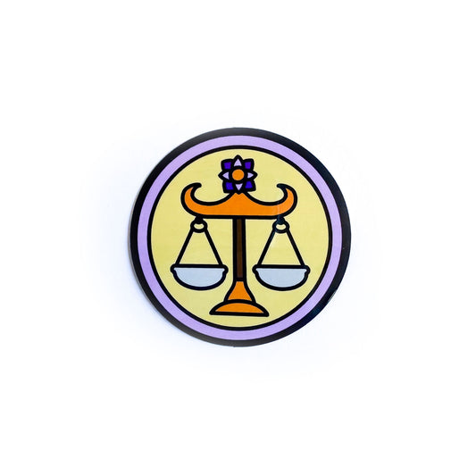 A sticker of a yellow circle with a lavender border with a cute drawing of the scales of justice representing the Libra zodiac sign in the center of the yellow circle.