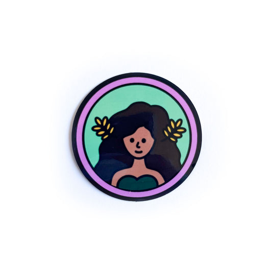A sticker of a woman with brown skin and flowing brown hair with wheat fronds in it, she is in a green circle with a lavender border. This is meant to represent the Virgo zodiac sign. 