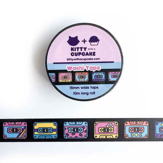 A circular roll of washi tape with a piece of the tape stuck below it. The washi tape has a black background and has a row of colorful cassette tapes along it.