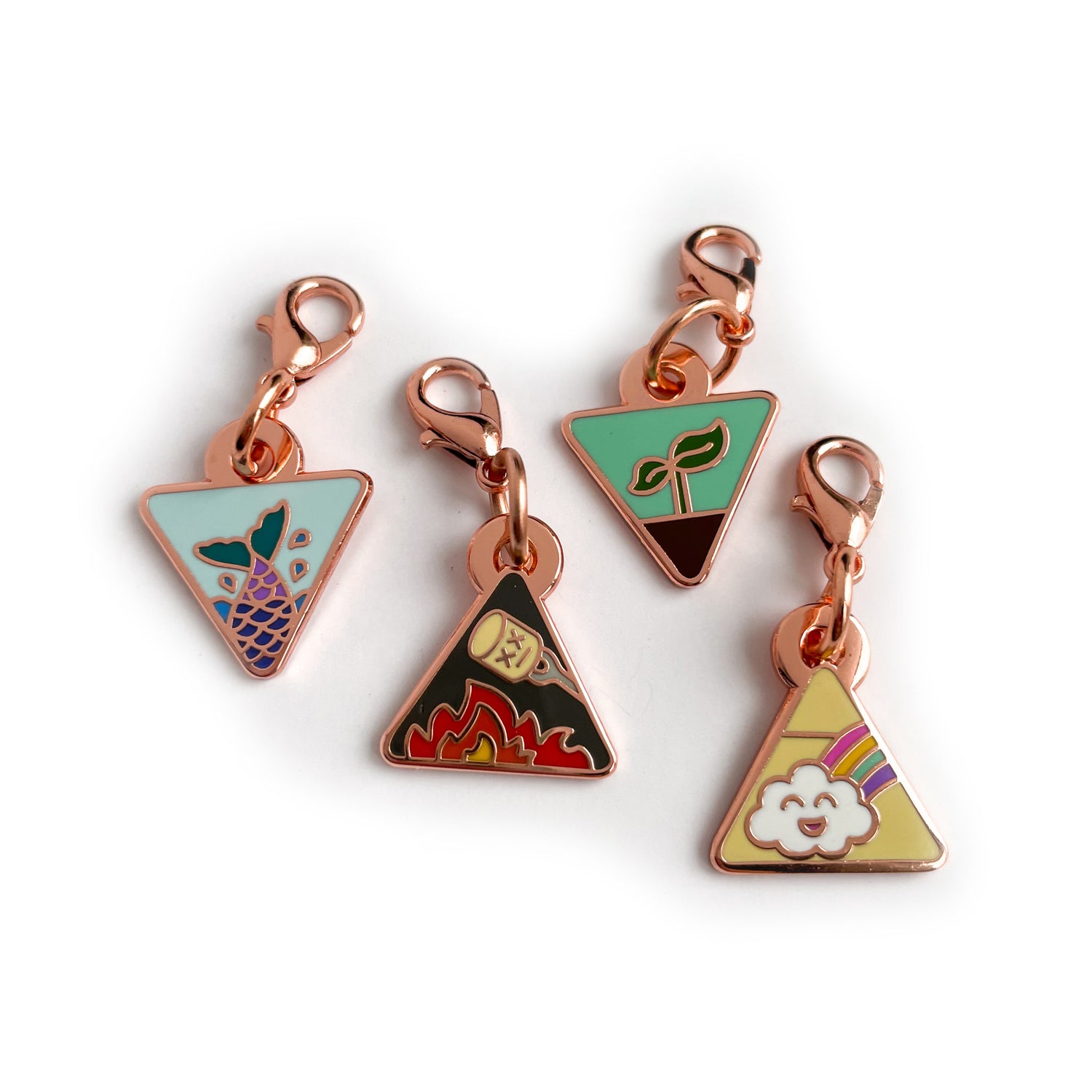 Four triangle shaped charms with lobster claw clasps. There is a mermaid tail charm, a fire with a marshmallow charm, a plant sprouting charm, and a happy rainbow cloud charm. 