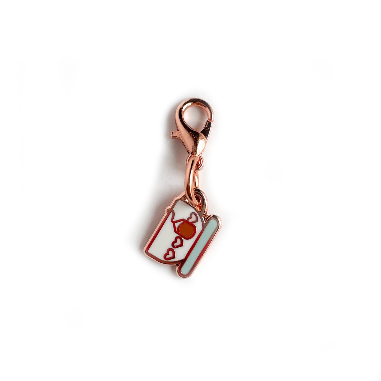 A charm on a lobster claw clasp that is shaped like a teacup with pink hearts on it and a teabag. 
