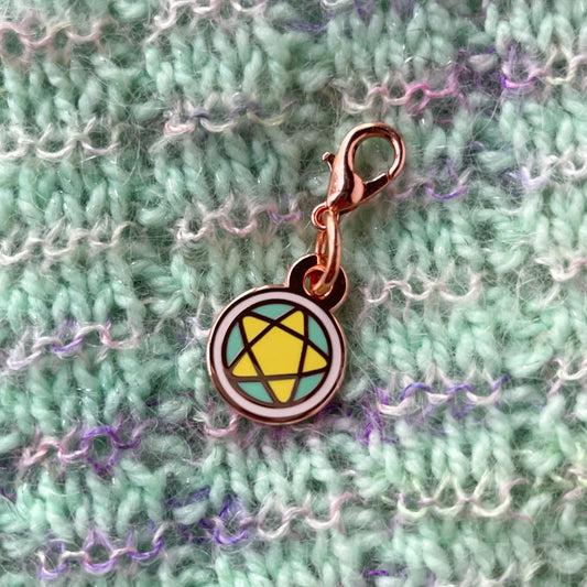 A pentacle charm on a background of hand knitted fabric. The fabric is mint green with stripes of pink fuzz.