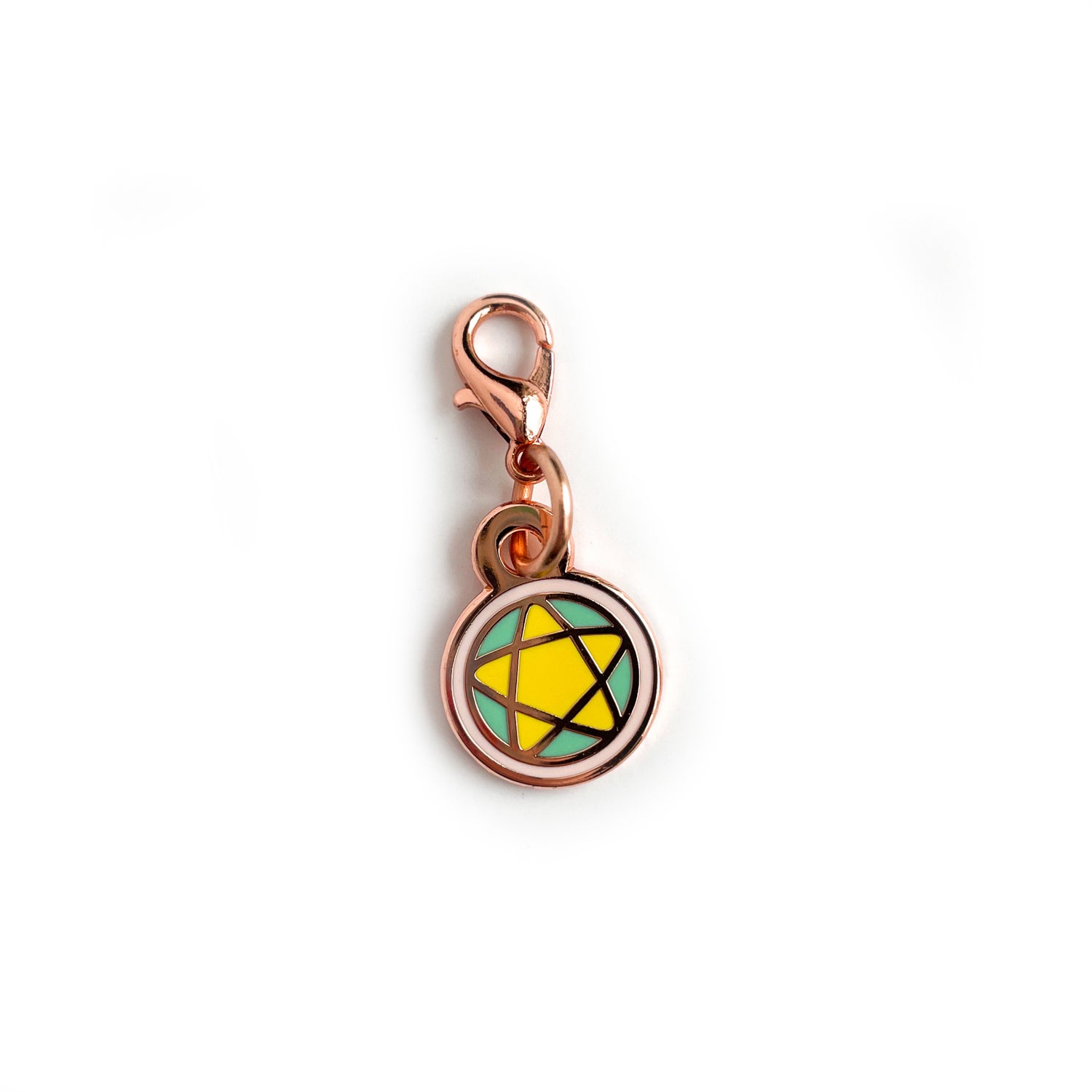 A lobster claw clasp charm of a pentacle in pastel colors and rose gold colored metal.