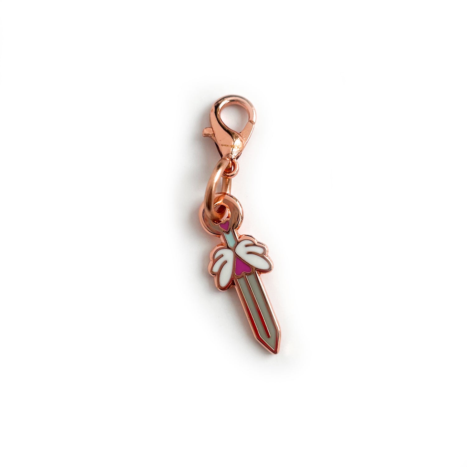 A charm with a lobster claw clasp in rose gold metal. The charm is shaped like a sword with heart and winged hilt.