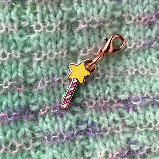 A star wand charm on a background of hand knit fabric. The fabric is mint green with fuzzy pink stripes.