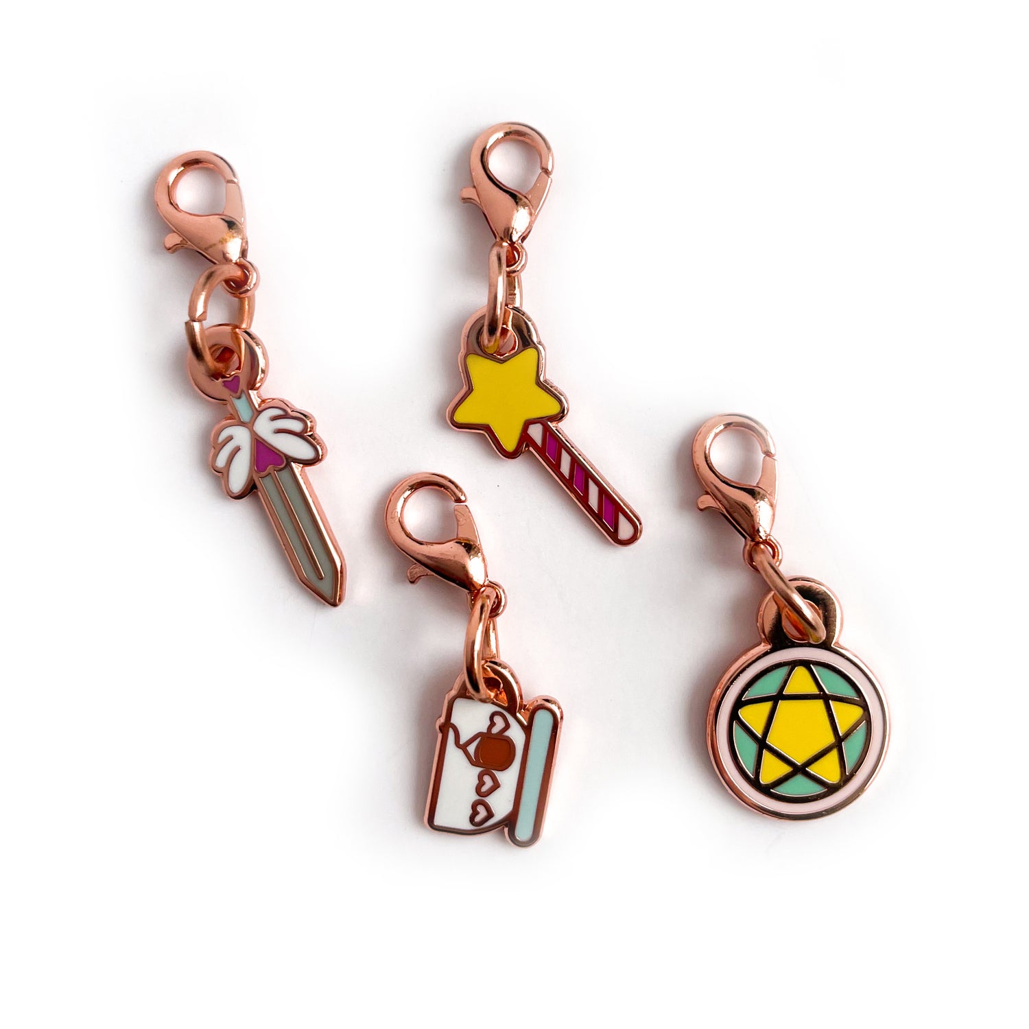A collection of charms on a white background. The charms are shaped like a sword, a teacup, a wand, and a pentacle circle.