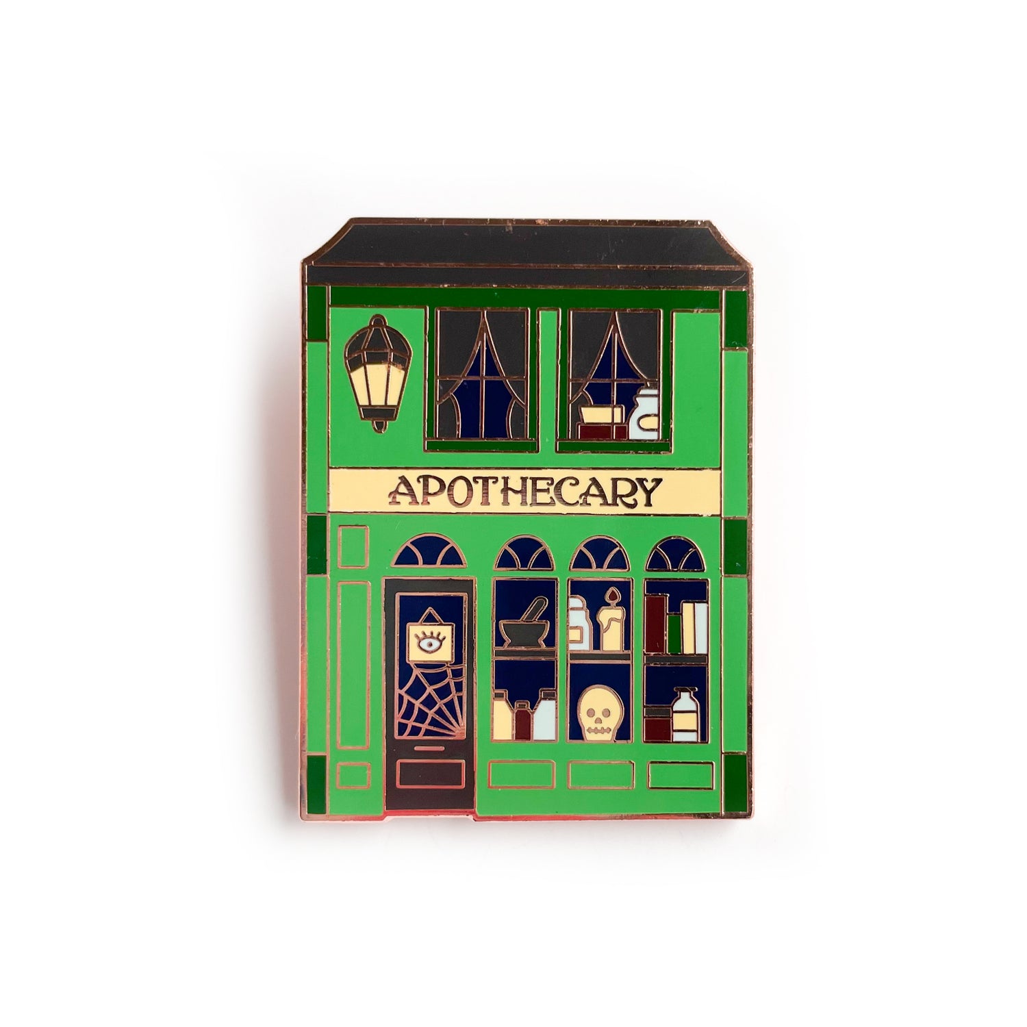 A pin shaped like a storefront with the word "Apothecary" across it. The windows of the shop are full of magic books, a skull, a candle, and a spiderweb