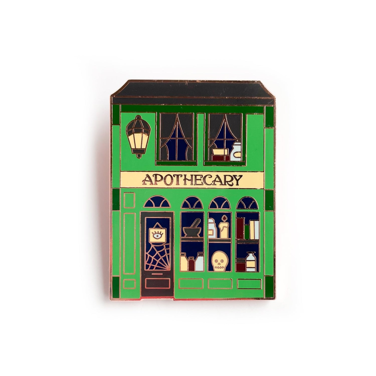 A pin shaped like a storefront with the word "Apothecary" across it. The windows of the shop are full of magic books, a skull, a candle, and a spiderweb