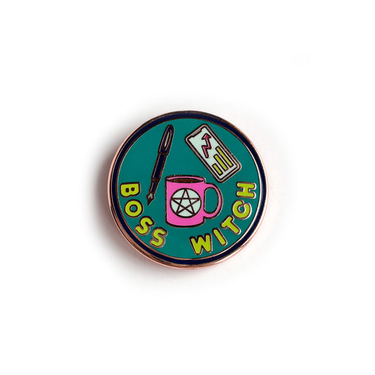 A circular enamel pin with copper details. It has a purple border with a turquoise background with lime green letters that read "Boss Witch". There is also a hot pink coffee cup with a pentacle, a purple fountain pen, and a phone with a graph on it.