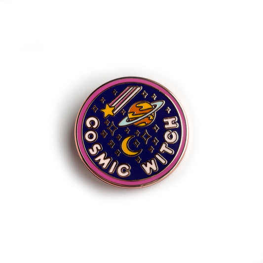 A circular enamel pin. It has a hot pink border, a navy background and light pink letters that read "Cosmic Witch." It also has stars, a crescent moon, a shooting star, and the planet Saturn depicted on it.