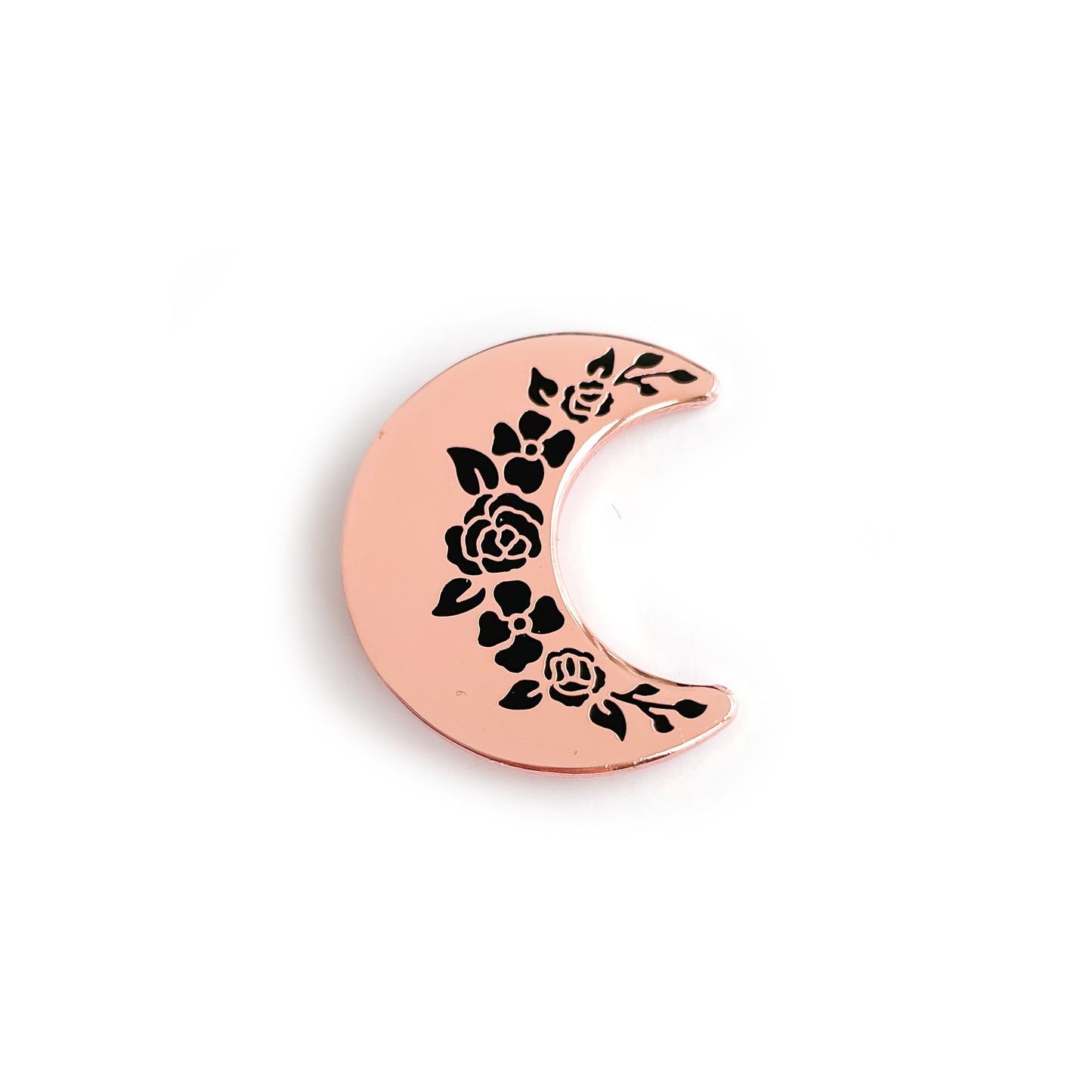 A crescent shaped enamel pin in rose gold metal with black floral shapes along the inside edge.