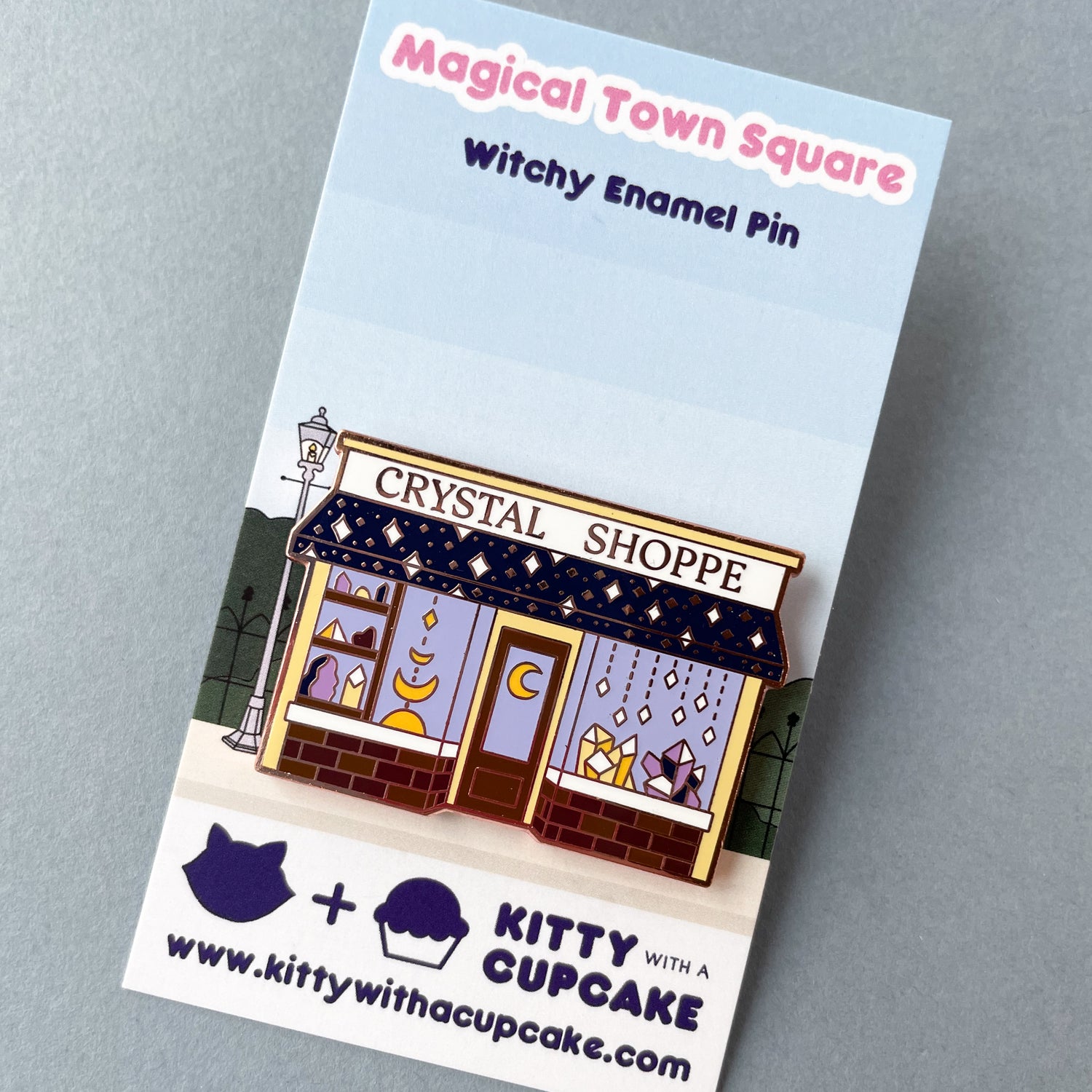 A Crystal Shoppe pin on a backing card that has an image of a street on it. 