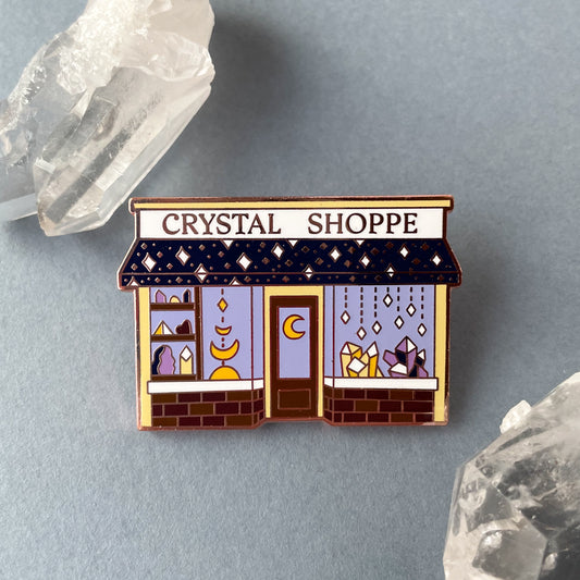 A Crystal Shoppe pin on a grey background surrounded by quartz crystals.