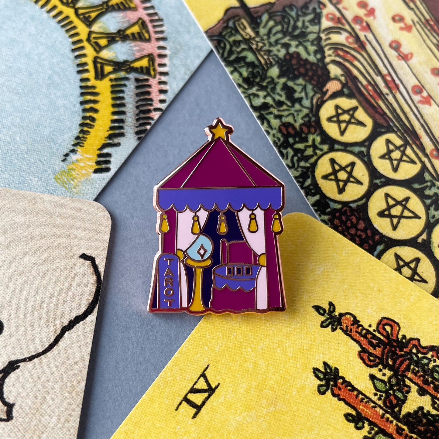 A tent shaped pin surrounded by cards from the Smith-Waite tarot deck.