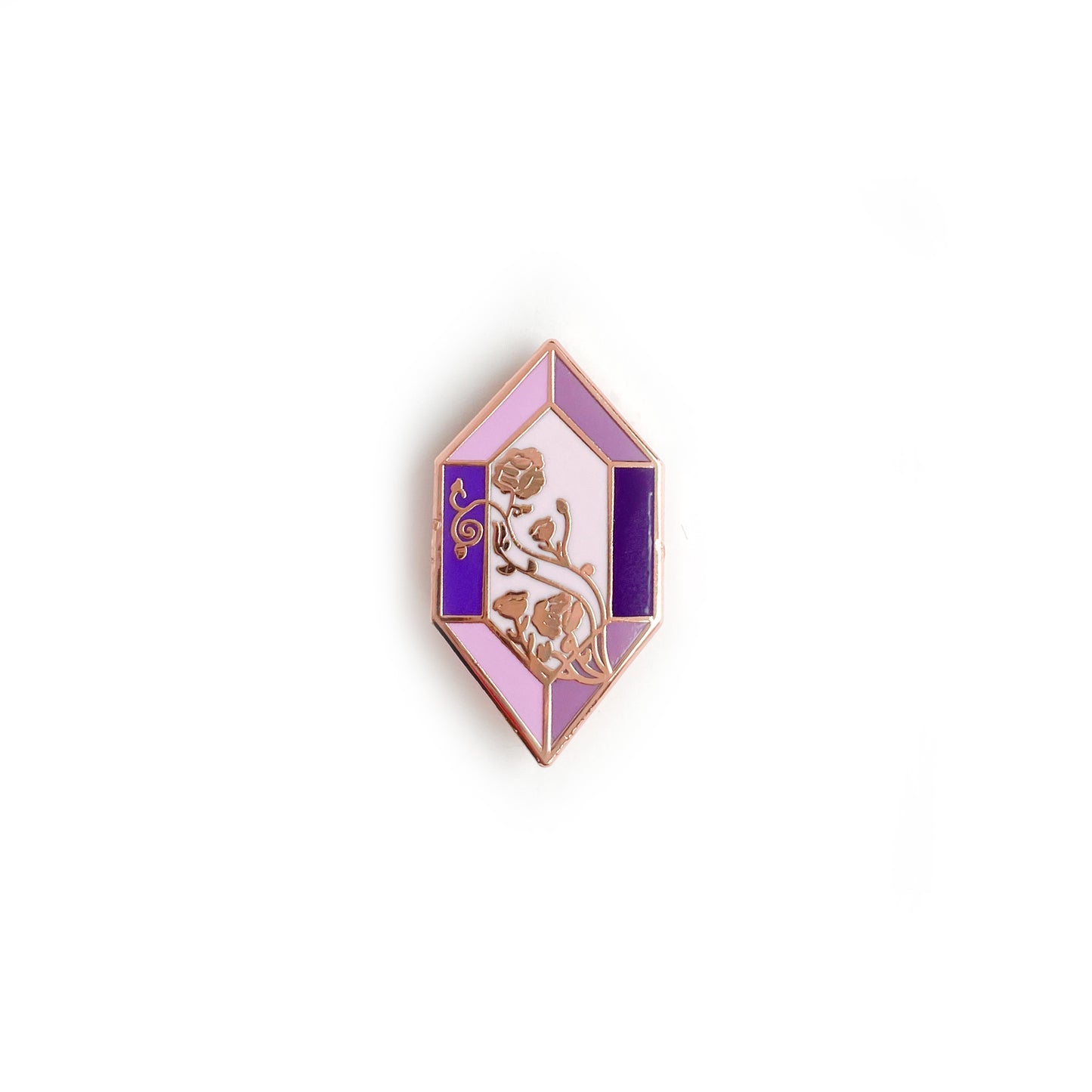 An elongated hexagon shaped enamel pin. It has rose gold colored metal and various shades of purple in the geometric panels to look like a gem. A floral line pattern crosses diagonally across the face of the gem.