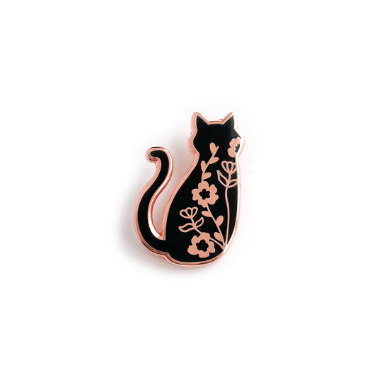 An enamel pin with rose gold metal that is in the shape of the back of a black cat. There are climbing floral vines along the cat's back.