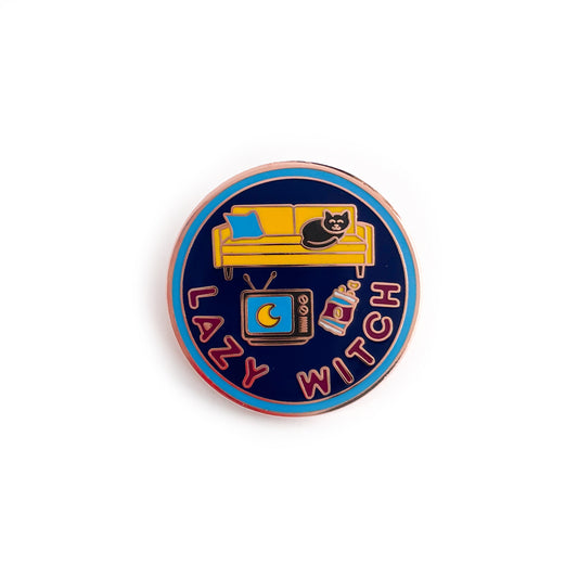 A circular enamel pin with a blue border, navy background, and maroon words that say "Lazy Witch". It has a vintage TV, bag of chips, a yellow couch and a black cat on the couch.