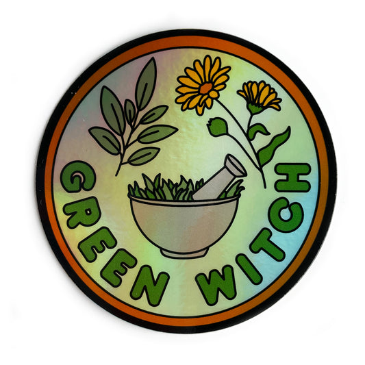 A circular holographic sticker that has an orange border and the words "Green Witch" on it. Sage leaves, calendula flowers, and a mortar and pestle are depicted on it. 