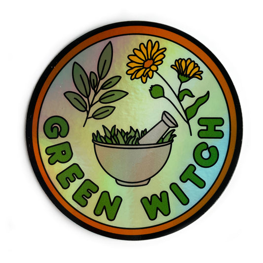 A circular holographic sticker that has an orange border and the words "Green Witch" on it. Sage leaves, calendula flowers, and a mortar and pestle are depicted on it.