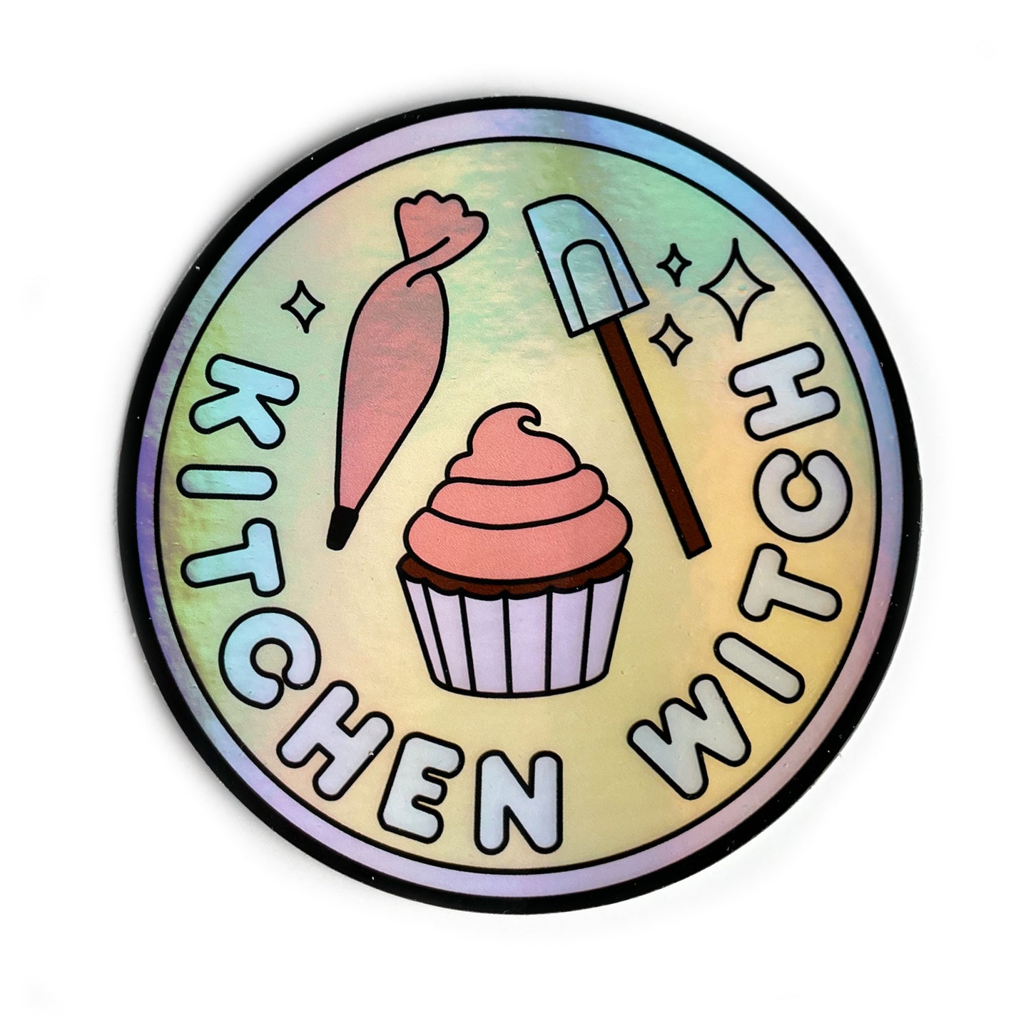 A circular holographic sticker with a lavender border and the words "Kitchen Witch" on it. It has a frosting piping bag, a cupcake, and a spatula on it.