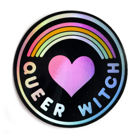 A circular holographic sticker with a black background and the words "Queer Witch" on it. It has a heart with a rainbow above it.
