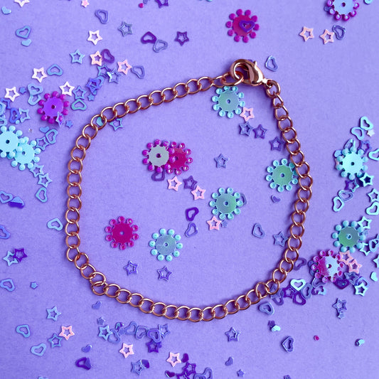 Copper charm bracelet on a lavender paper background covered in confetti