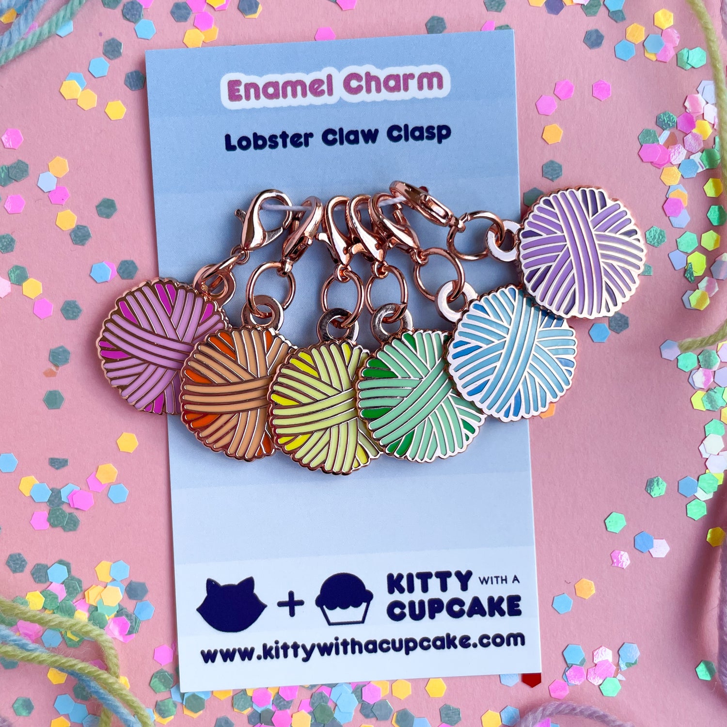Six lobster claw clasp charms shaped like yarn balls in pink, orange, yellow, mint, blue, and purple on blue card. 