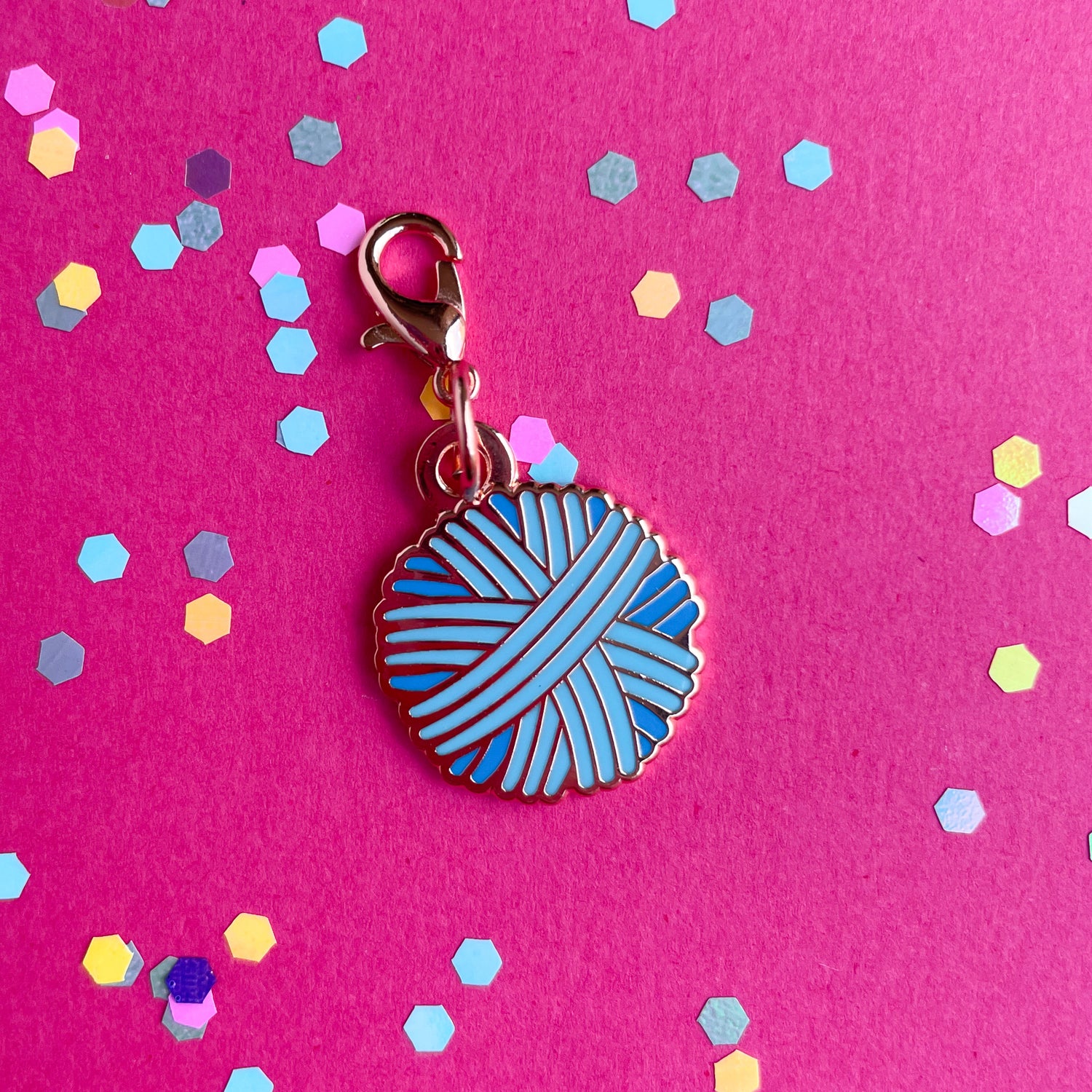 A pastel blue yarn ball charm on a hot pink background with confetti