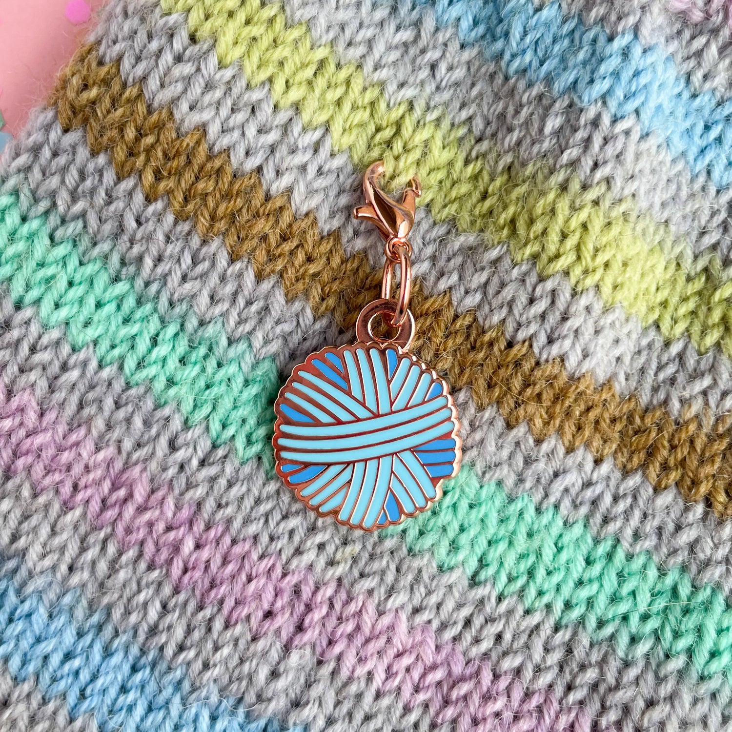 A pastel blue yarn ball charm on a hand knit background.
