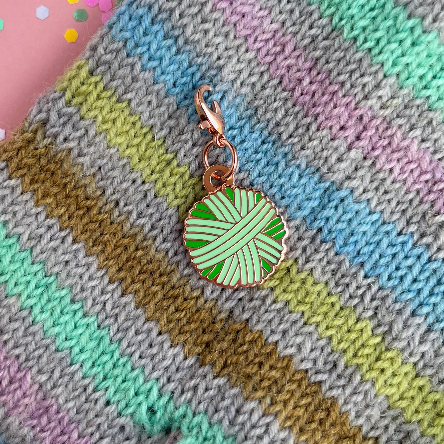 A mint green yarn ball charm on a knit background