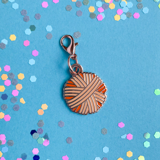 A yarn ball shaped lobster claw clasp charm on a blue paper background with confetti on it.