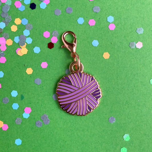 A purple yarn ball charm on a green background with confetti.