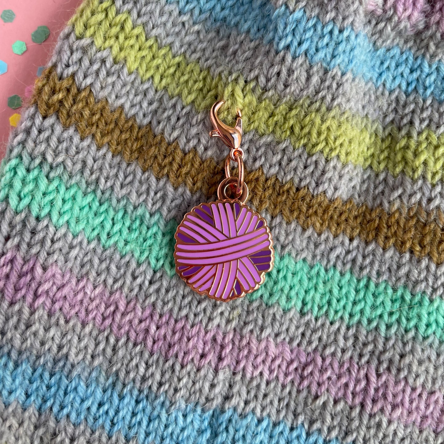 A purple yarn ball charm on a hand knit background.