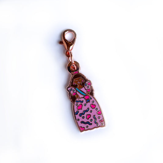 An enamel charm with a lobster claw clasp shaped like a birthday barbie doll with caramel skin and brown hair.