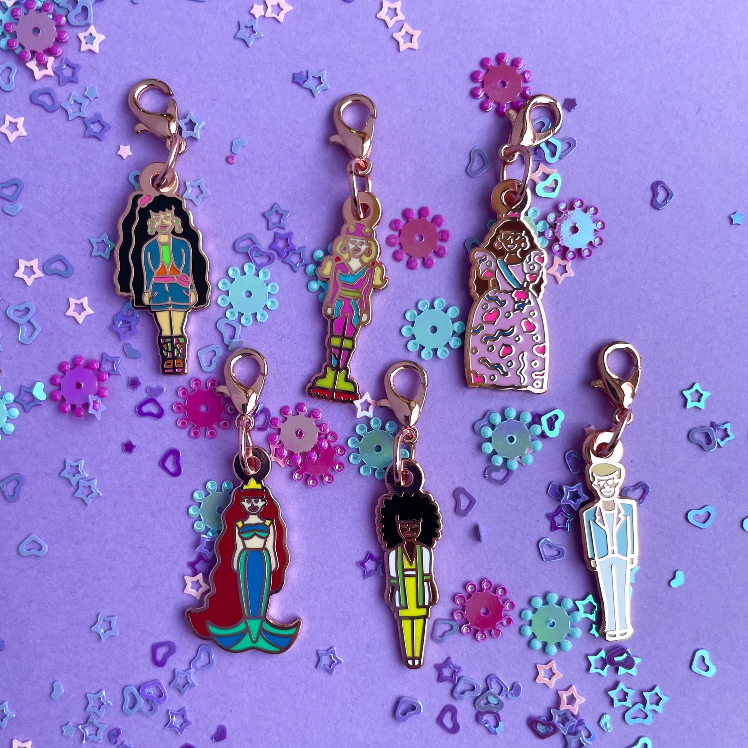Six doll shaped charms on a lavender paper background covered in confetti