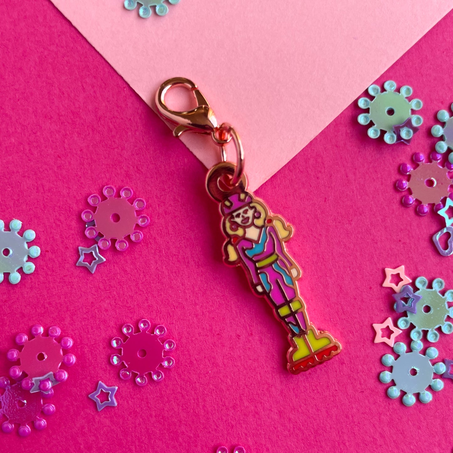 An enamel charm shaped like a barbie with pigtails wearing helmet and rollerblades on a pink paper background.