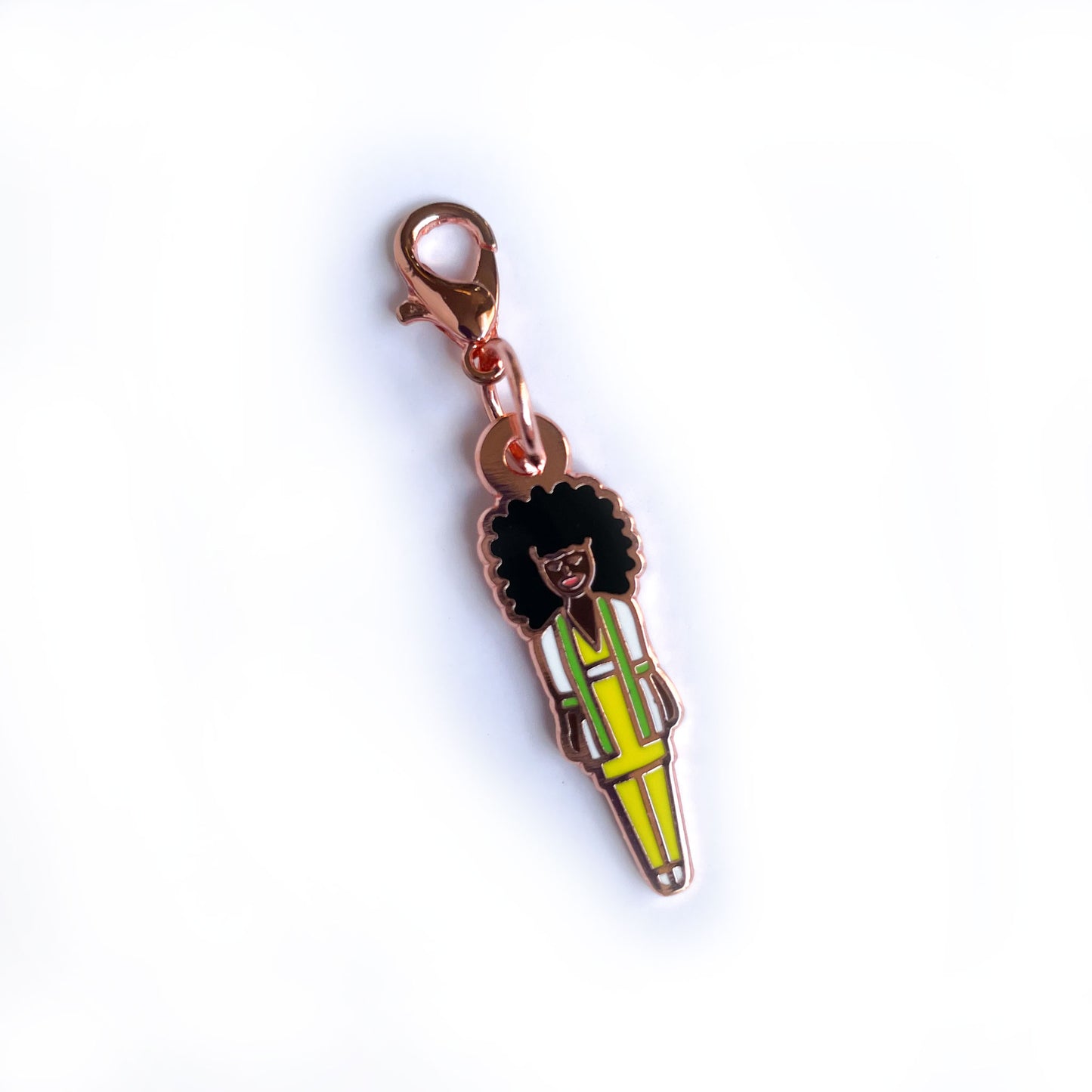 An enamel charm shaped like a barbie doll with dark brown skin and an afro in a yellow suit. 