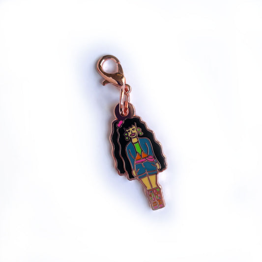 An enamel charm shaped like a barbie with long dark black hair wearing 90s clothes.