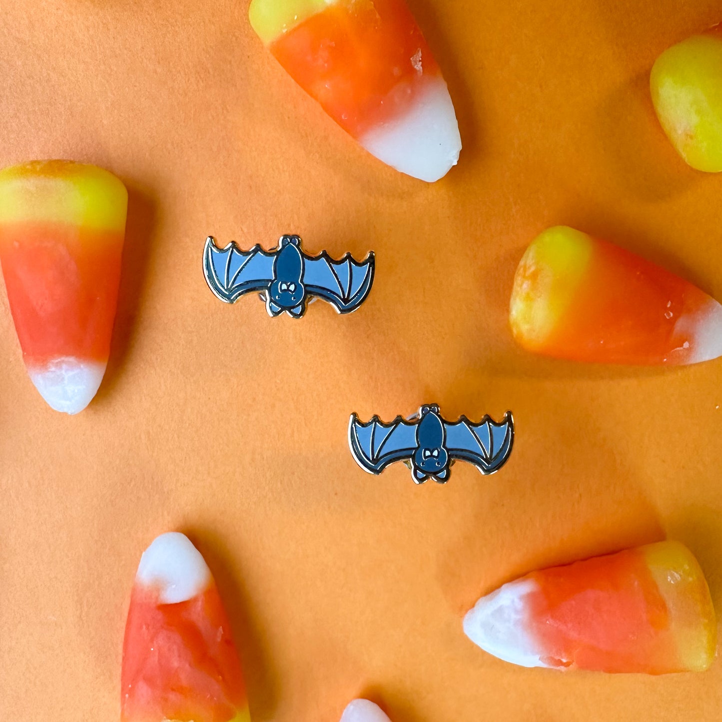 Upside down bat earrings on orange paper surrounded by candy corn