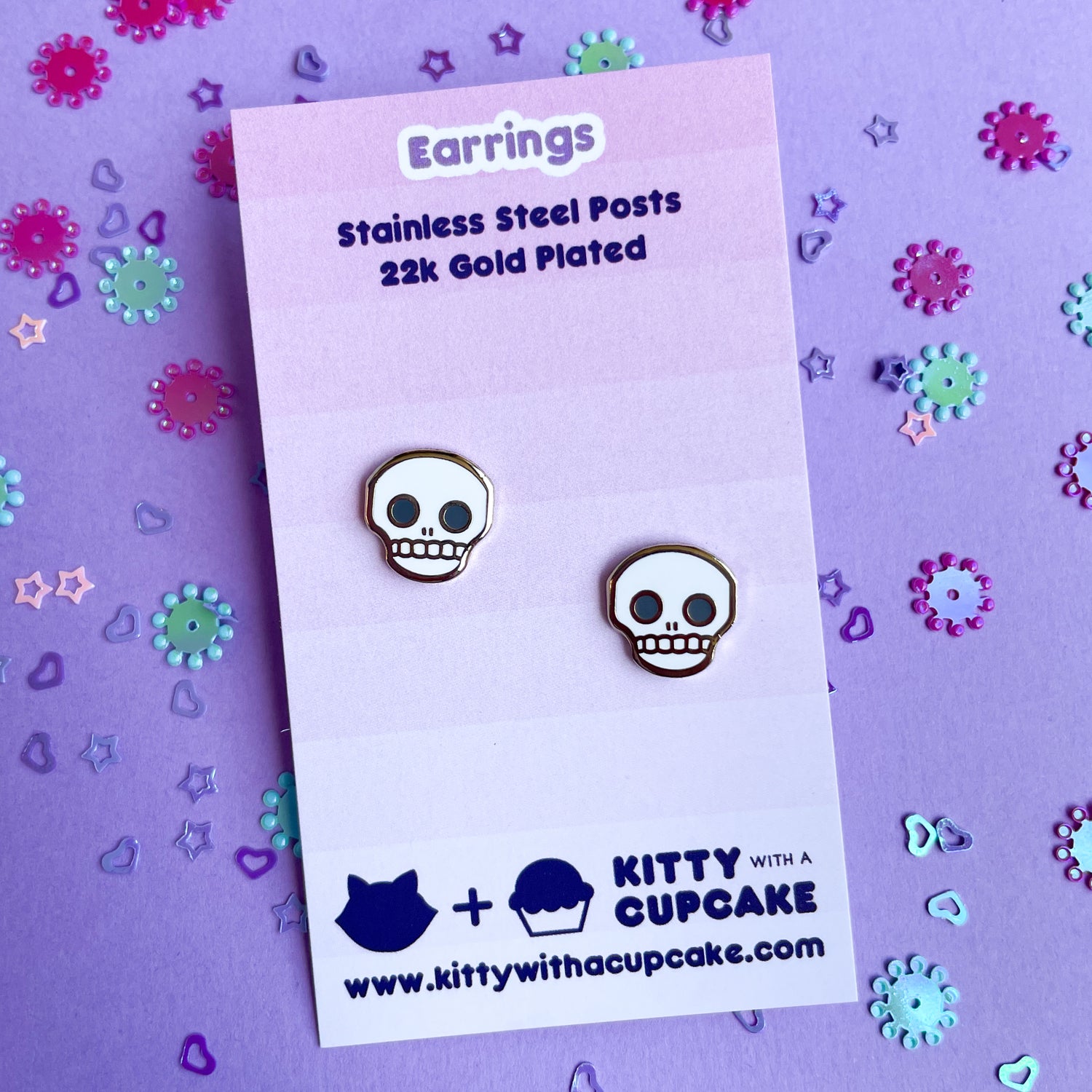 Skull stud earrings on a pink card. 